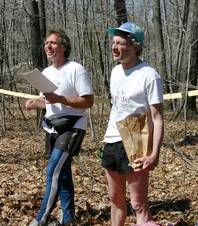 The two men stand in front of the string from which result cards hang.